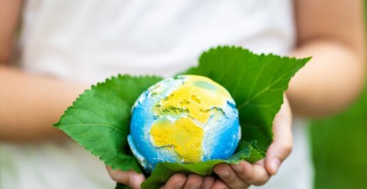 Child holding small planet in hands against spring or summer green background. Ecology, environment and Earth day concept. High quality photo